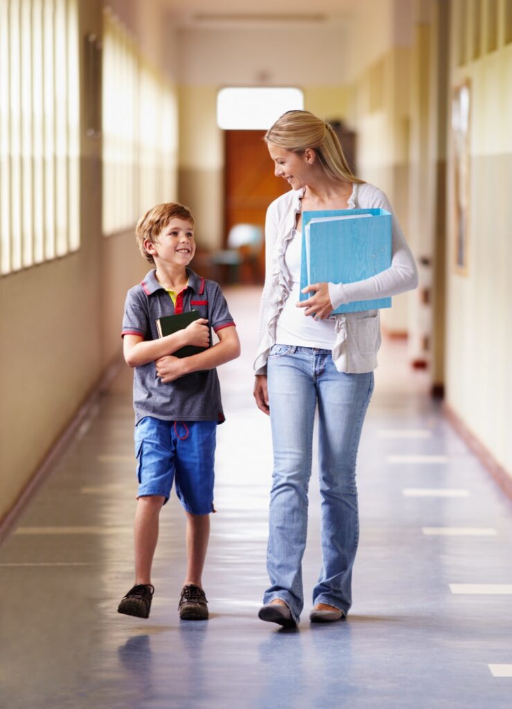 A teacher and young boy walking together down the corridor